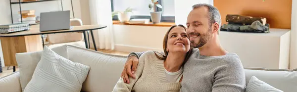 Hombre feliz con los ojos cerrados abrazando a la esposa en el sofá en la sala de estar, pareja sin hijos, pancarta - foto de stock