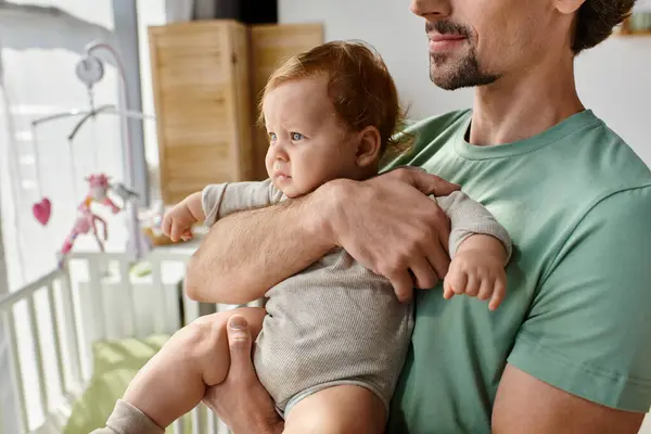Обрізаний знімок бородатого батька тримає в руках свого немовляти сина в затишній спальні вдома, батьківство — стокове фото