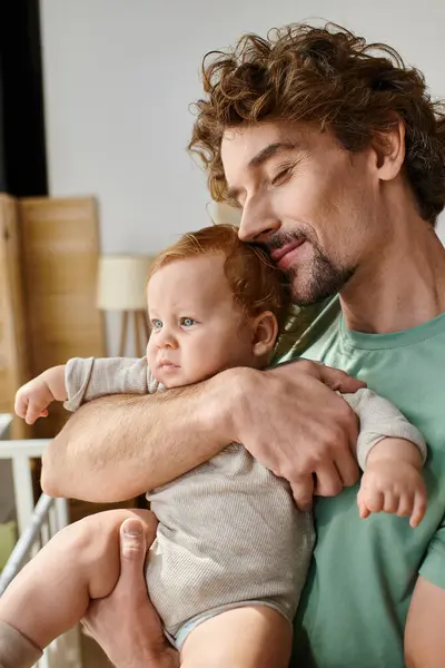 Кучеряве волосся і веселий батько тримає в руках свого немовляти сина в затишній спальні вдома, батьківство — стокове фото