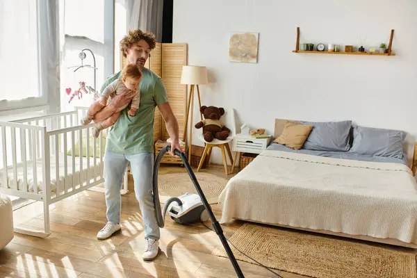 Mann Multitasking Hausarbeit und Kinderbetreuung, Vater staubsaugt Hartholzboden mit Säugling im Arm — Stockfoto