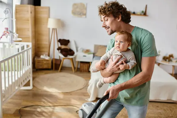 Homem multitarefa trabalho doméstico e puericultura, pai aspirando piso de madeira dura com bebê filho nos braços — Fotografia de Stock