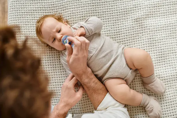 Top view of single father giving pacifier to his infant baby son on the bed, fatherhood and love — Stock Photo