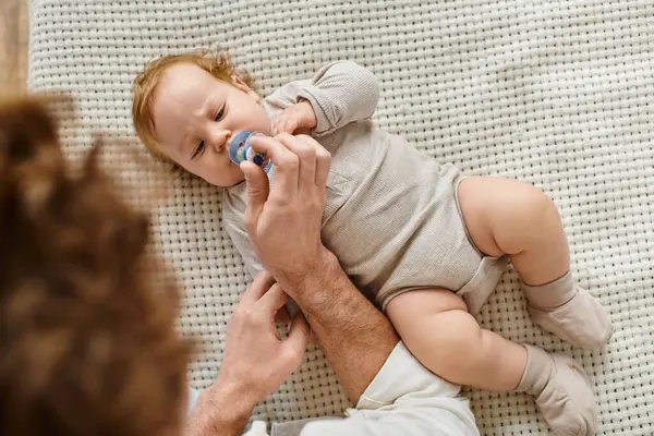 Vue du dessus du père célibataire donnant la sucette à son bébé fils sur le lit, la paternité et l'amour — Photo de stock