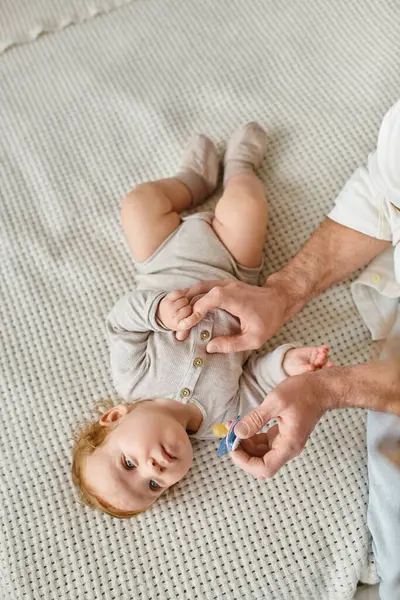 Top view of infant child looking at his blurred father with pacifier in hand, fatherhood and love — Stock Photo