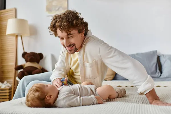 Joyeux père célibataire donnant sucette à son bébé fils sur le lit, la paternité et l'amour — Photo de stock