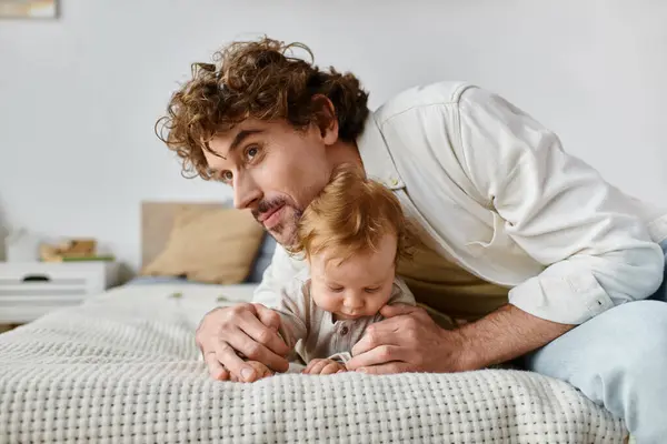 Padre protettivo con i capelli ricci abbracciare il suo bambino mentre sdraiati insieme sul letto, prezioso — Foto stock