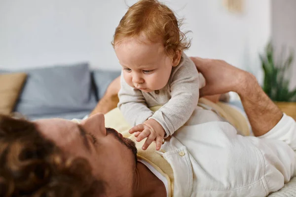 Cute infant boy outstretching hands towards bearded dad on a bed, bonding between father and son — Stock Photo