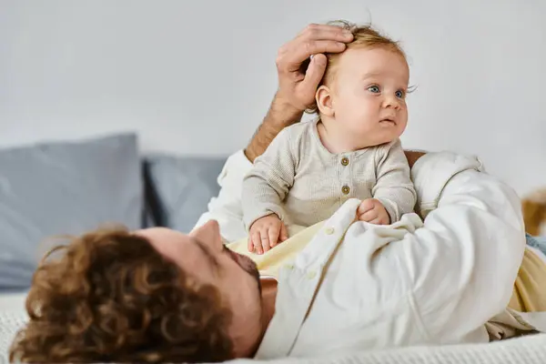 Single father with curly hair and beard stroking hair of his infant son in bedroom, love and care — Stock Photo