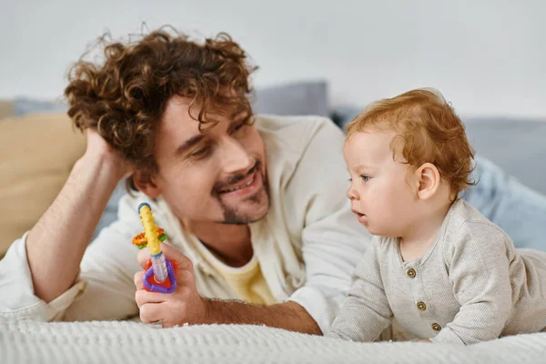 Felice uomo mostrando sonaglio colorato per neonato in camera da letto, legame tra padre e figlio — Foto stock