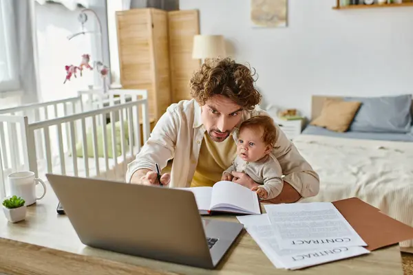 Homem segurando nos braços seu filho bebê enquanto toma notas e trabalhando em casa, equilíbrio vida-trabalho — Fotografia de Stock