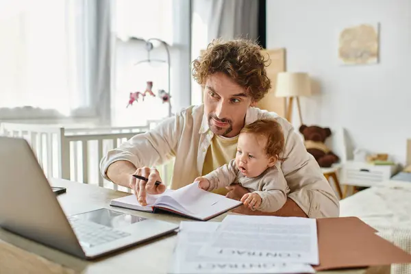 Чоловік тримає в руках свого немовляти сина, працюючи дистанційно на ноутбуці з дому, баланс робочого життя — стокове фото
