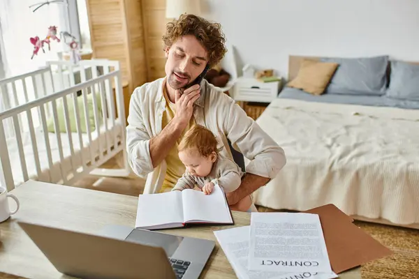 Padre che tiene in braccio il figlio neonato mentre parla su smartphone e lavora da casa, equilibrio lavoro-vita privata — Foto stock