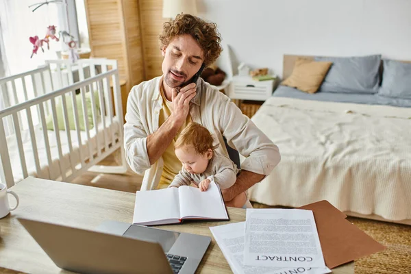 Père tenant son fils en bas âge tout en parlant sur smartphone et en travaillant à la maison, équilibre travail-vie privée — Photo de stock