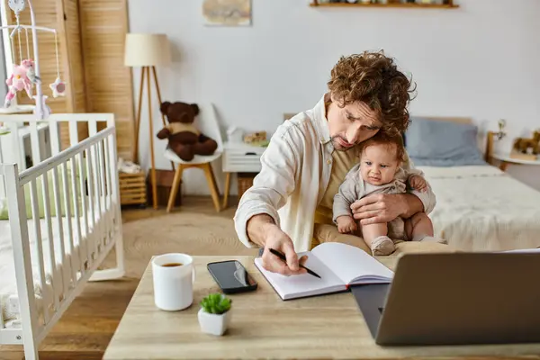 Занятой отец-одиночка держит своего грустного младенца в руках, работая из дома, баланс между работой и жизнью — стоковое фото