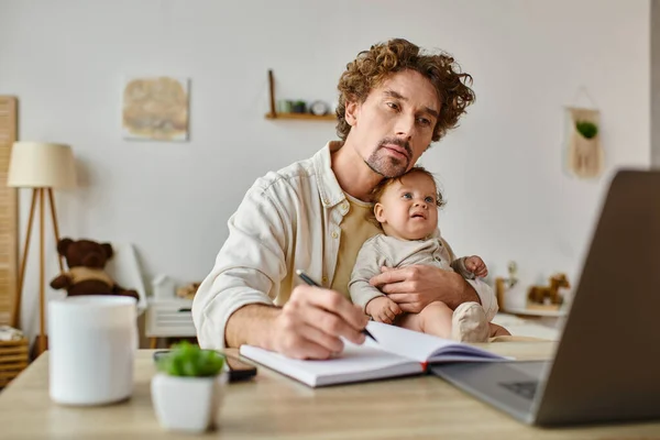 Ocupado pai solteiro segurando seu filho bebê nas mãos enquanto trabalhava em casa, equilíbrio vida-trabalho — Fotografia de Stock