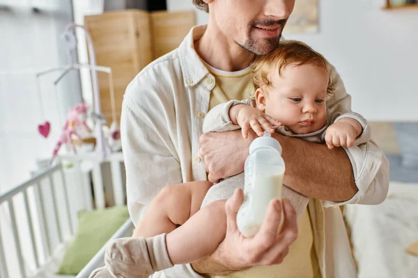 Beschnitten Vater füttert seinen kleinen Sohn aufmerksam mit Milch in Babyflasche, Vaterschaft und Pflege — Stockfoto