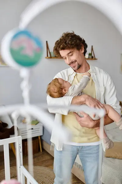 Felice padre single che tiene in braccio il figlio neonato vicino alla culla in asilo nido, paternità e amore — Foto stock