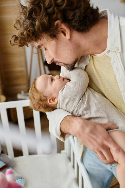 Caring single father lifting his infant son from baby crib in nursery, fatherhood and love — Stock Photo