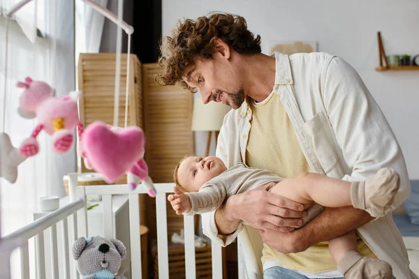 Carinhoso e feliz pai levantando seu filho bebê berço no berçário, paternidade e amor — Fotografia de Stock