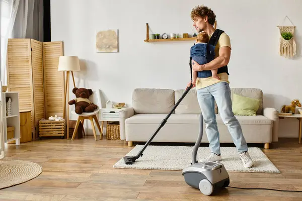 Bearded man with infant baby boy in carrier vacuuming apartment at home, cleanliness and housework — Stock Photo