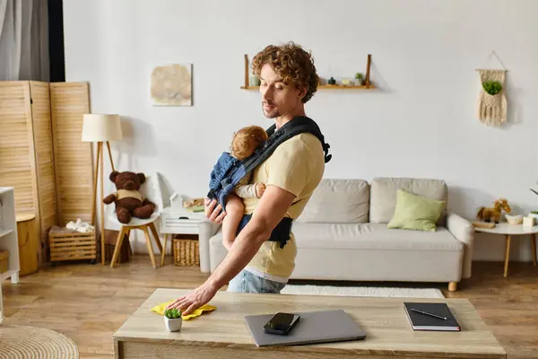 Padre riccio con figlio neonato in portante asciugatura tavolo con straccio giallo vicino a gadget e minuscola pianta — Foto stock