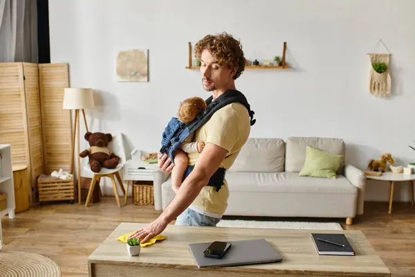 Padre rizado con hijo pequeño en la mesa de limpieza portadora con trapo amarillo cerca de gadgets y plantas diminutas - foto de stock