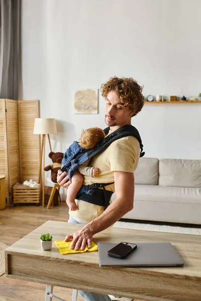 Padre occupato con figlio neonato nel tavolo di pulitura portante con straccio giallo vicino a gadget e minuscola pianta — Foto stock
