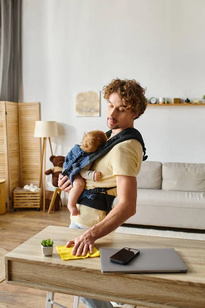 Padre ocupado con hijo pequeño en la mesa de limpieza portadora con trapo amarillo cerca de gadgets y plantas diminutas - foto de stock