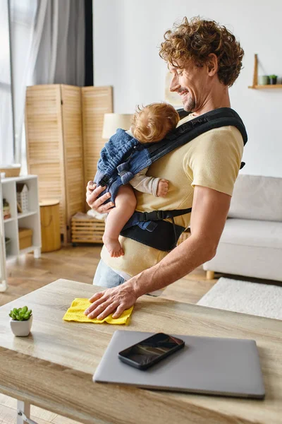 Felice padre con figlio neonato nel tavolo di pulitura vettore con straccio giallo vicino a gadget e minuscola pianta — Foto stock