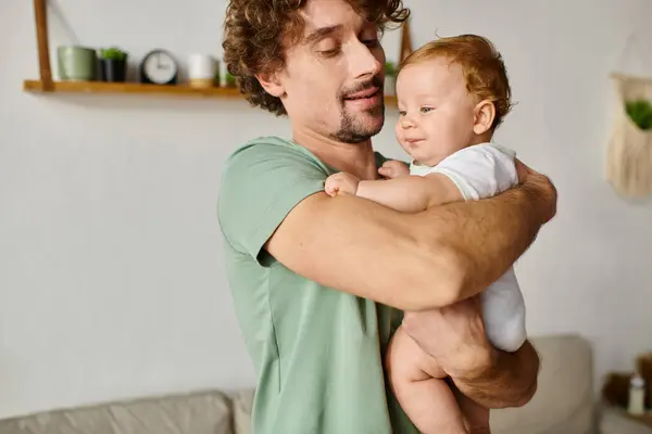 Joyeux père avec la barbe tenant dans les bras son fils bébé souriant dans un salon confortable, portrait — Photo de stock