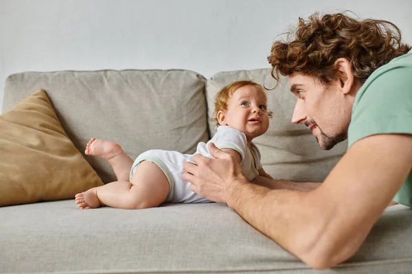 Father looking at cute infant baby son and having a happy moment on sofa in living room, parenting — Stock Photo