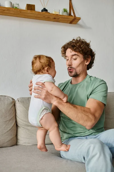 Отец держит в руках милый младенец маленький сын и счастливый момент на диване в гостиной — стоковое фото
