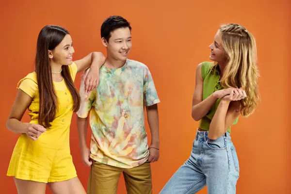 Adorabile jolly diversi adolescenti in abiti vibranti guardando l'un l'altro sullo sfondo arancione — Foto stock