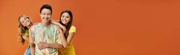 Alegre diversa adolescentes en vibrantes trajes sonriendo a la cámara en el fondo naranja, día de la amistad, bandera - foto de stock