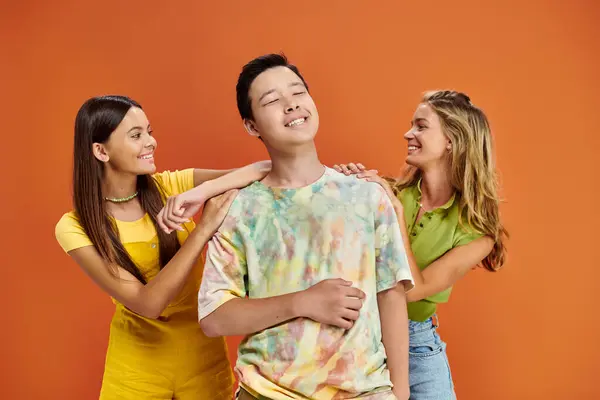 Allegri adolescenti multirazziali in abiti vivaci divertirsi insieme sullo sfondo arancione, giorno dell'amicizia — Foto stock