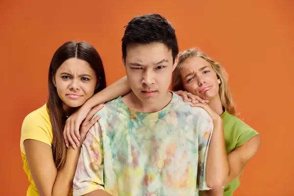 Confused interracial teenagers in vivid attires looking at camera on orange backdrop, friendship day — Stock Photo