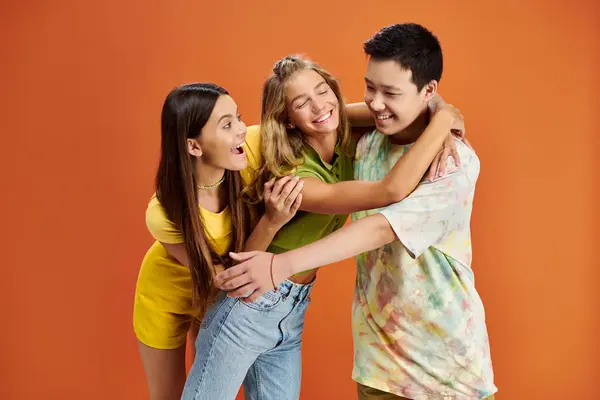 Gioiosi adolescenti multirazziali in abiti luminosi che si abbracciano su sfondo arancione, giorno dell'amicizia — Foto stock