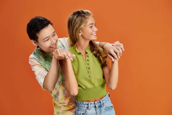 Jolly multiracial friends in vivid clothes hugging and looking away on orange backdrop, friendship — Stock Photo
