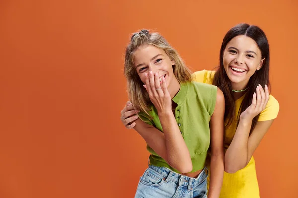 Gioiose adorabili ragazze adolescenti che abbracciano e sorridono alla macchina fotografica sullo sfondo arancione, giorno dell'amicizia — Foto stock