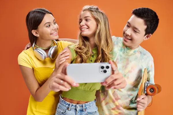 Joyeux divers amis dans des vêtements vifs prendre selfie et sourire à l'autre sur fond orange — Photo de stock