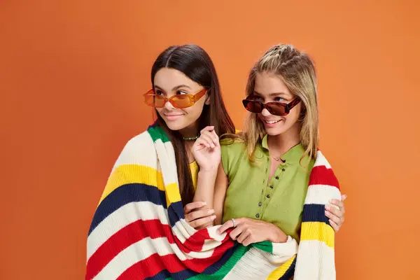 Joyous adorable teens with sunglasses covering with blanket and looking away, friendship day — Stock Photo