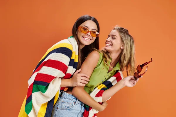 Happy pretty teenage girls with sunglasses hugging and having great time on orange backdrop — Stock Photo