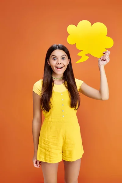 Gioiosa adolescente in posa con bolla di pensiero in mano e guardando la fotocamera su sfondo arancione — Foto stock
