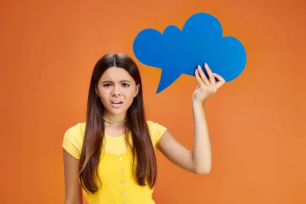 Confused adorable teenager in everyday vivid outfit holding thought bubble and looking at camera — Stock Photo