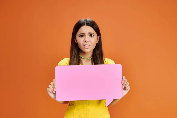 Scared and confused teenage girl in casual attire holding speech bubble and looking at camera — Stock Photo