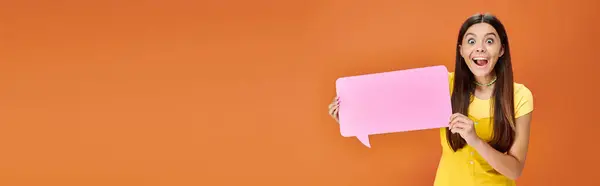 Cheerful adolescent girl in vibrant attire holding speech bubble and looking at camera, banner — Stock Photo