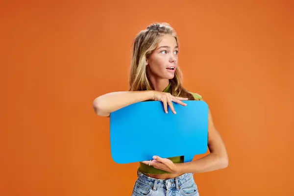 Cheerful teenage girl in casual vivid attire with speech bubble looking away on orange backdrop — Stock Photo
