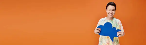 Joyous asian teenage boy in vivid attire holding blue thought bubble and looking at camera, banner — Stock Photo