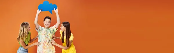 Jolly diverse teens posing with blue thought bubble on orange backdrop, friendship day, banner — Stock Photo