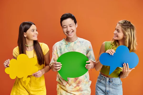 Joyful adolescent interracial friends holding speech and thought bubbles on orange background — Stock Photo